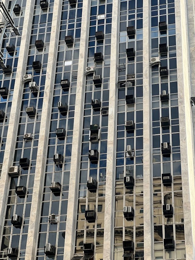 Multiple AC external units and ventilation systems on a high-rise glass building facade, demonstrating Smart Agnes's expertise in large-scale HVAC installation and maintenance in Qatar.