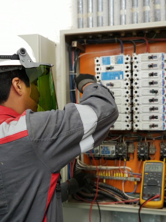 Professional electrical engineer in full PPE testing an LV panel and circuit breakers with a multimeter, showcasing Smart Agnes’s expert electrical and power solutions in Qatar.
